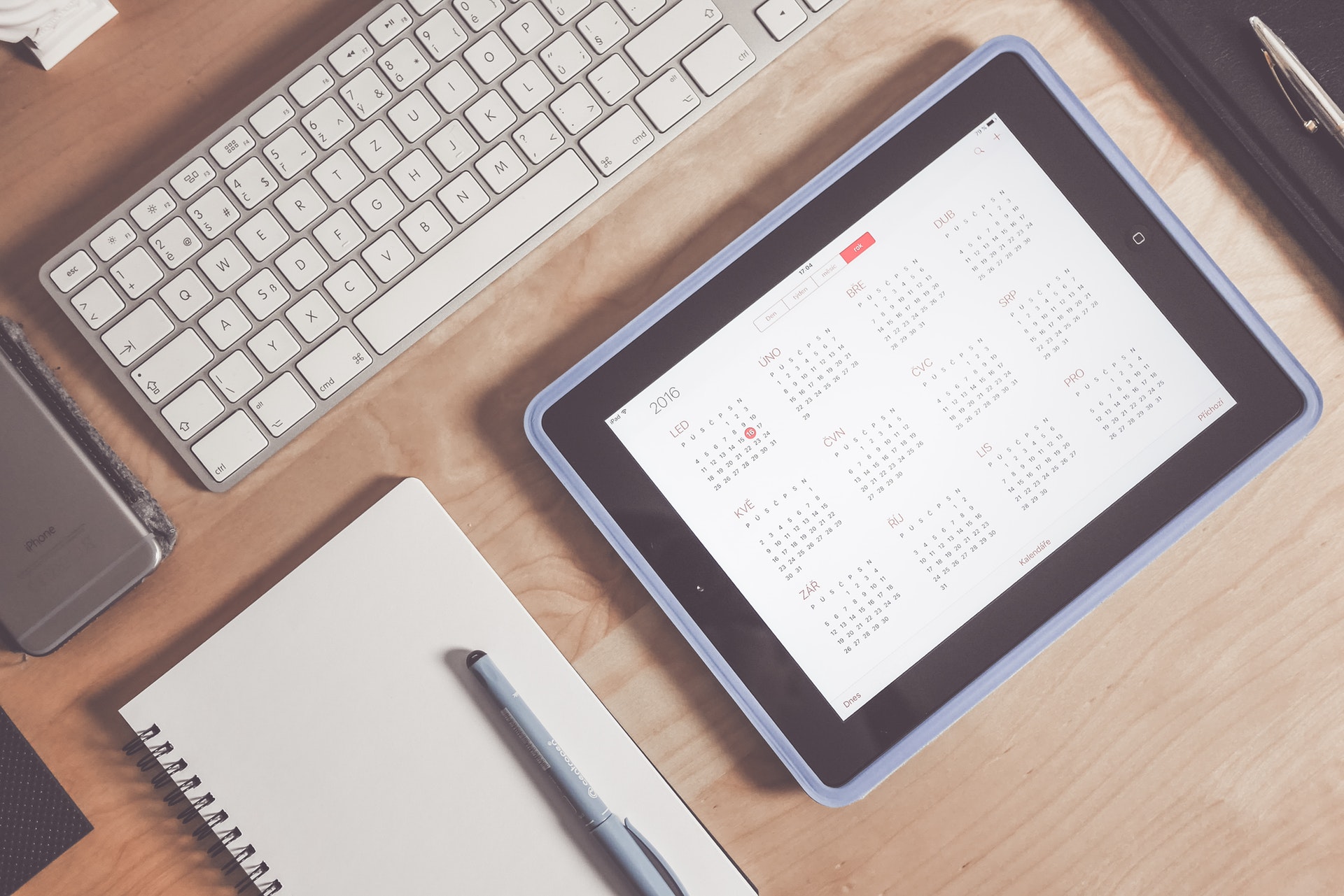 Ipad with calendar app open next to keyboard and apple computer